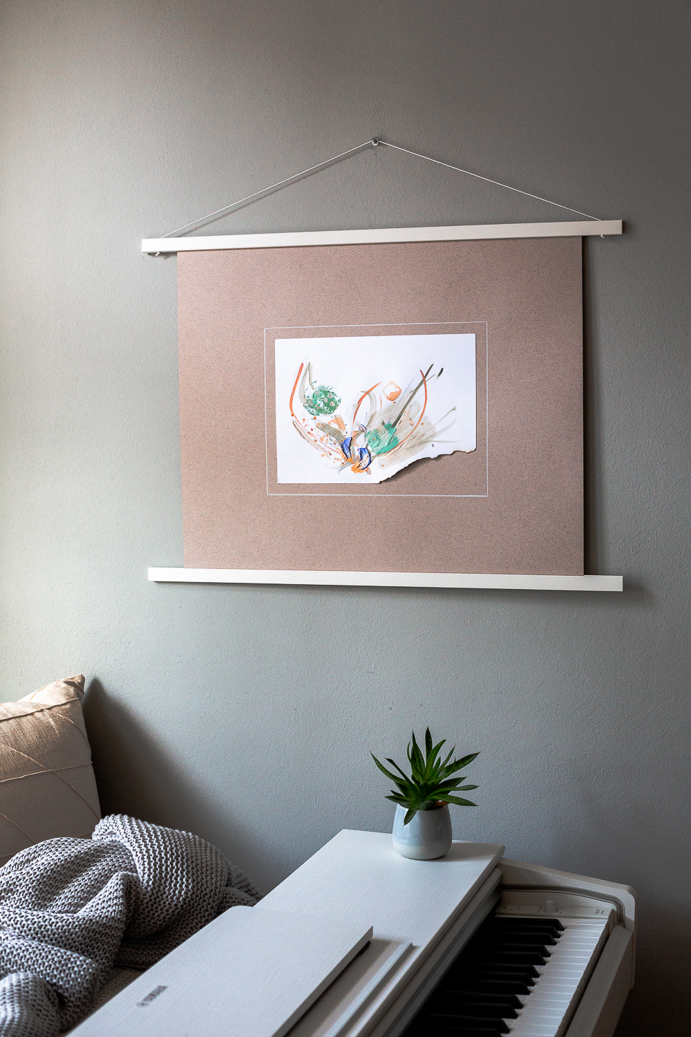 compassion i is an original abstract artwork by Rose Reichart. Here it is featured in a home with modern interior design in neutral shades. The intuitive painting is mounted on a blush colored paper and hangs on the wall with a white magnetic poster frame. Muted colors in tones of mint, peach, sage, beige and gray are present in the piece.